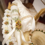 Decorative floral baptism crown with white and gold flowers placed on greenery.