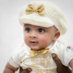 Close-up of baby wearing handmade crochet baptism hat with gold satin bow.