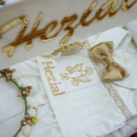 Baby boy smiling in embroidered personalized baptism romper with crochet hat.