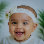 Smiling baby girl wearing a handcrafted ivory lace baptism headband with floral embellishments