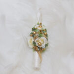 Handcrafted baptism candle decorated with white flowers, gold berries, and greenery on soft ivory fur background