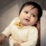 Baby in custom satin baptism romper with golden bow and floral hand embroidery
