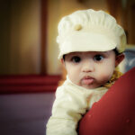 Baby wearing premium cream baptism cap with lace and golden button