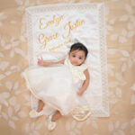 Baby girl in baptism dress with floral satin rose on personalized quilt