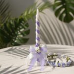 A handmade white and lavender spiral christening candle with a matching floral tiara set by Navin Creations, elegantly displayed for a baptism ceremony in Kochi.