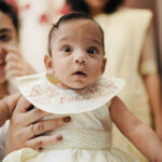 Baby wearing personalized baptism dress embroidered with angels and name “Esther” — handcrafted christening gown by Navin Creations, India.