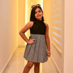 Girl wearing a black top and white checkered pleated dress posing confidently in a modern hallway