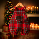 Red plaid Christmas baby romper hanging on a wooden hanger with warm festive background