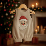 Off-white Christmas baby romper with embroidered Santa face hanging on a wooden hanger