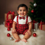 Baby boy Christmas tartan suspender romper with bow tie sitting near tree