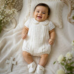 Baby boy wearing white baptism romper with Peter Pan collar, lace detailing, and matching booties