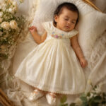 Sleeping baby girl in ivory christening dress with floral neck embroidery