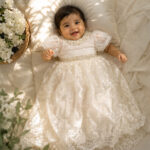 Baby girl wearing a white lace baptism gown with pearl work and puff sleeves