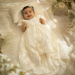 Baby girl wearing long lace christening gown with bow and headband