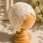 White lace baptism cap with floral embroidery and scalloped edge on wooden mannequin