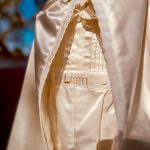 Close-up of Liam embroidered on an ivory satin baby boy baptism romper with pintuck detailing.