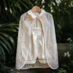 Luxury ivory baby boy christening romper displayed with a floral embroidered lace baptism cape.