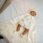 Baby boy wearing a personalised ivory baptism romper with satin cape, bonnet and booties.