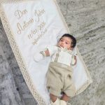 Baby boy wearing a beige and ivory christening outfit on a personalised baptism quilt embroidered with name and baptism date.
