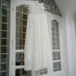 Long white baptism gown for baby girl featuring pearl embellished bodice, delicate floral embroidery and flowing lace skirt.